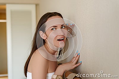 Woman eavesdropping through the wall of the room through a glass cup, curiosity, espionage, surprised face, vivid emotions Stock Photo