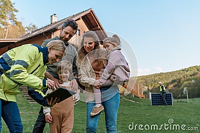 Woman engineer talking to young family about solar panel installation in front of their house. Stock Photo