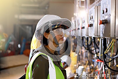 Woman Engineers electrical control with safety helmet and safety glasses for industrial estate or power plant background. Industry Stock Photo