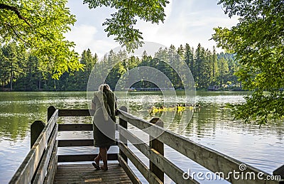 Woman enjoying lake view in forest standing on wooden pier Editorial Stock Photo