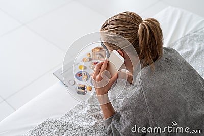 Woman with face mask relaxing lying on the bed reading a magazine ordering food Stock Photo