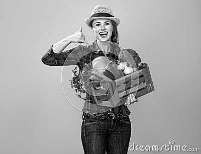 Woman farmer with box of vegetables showing call me gesture Stock Photo