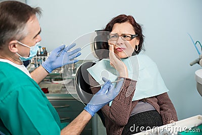Woman feeling toothache, touching cheek with hand at dental clinic. Senior dentist trying to help Stock Photo
