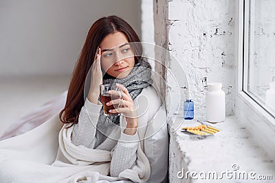 Woman feels a headache and holds her hand to her head. Close up of beautiful young woman in warm plaid with hot cup of Stock Photo