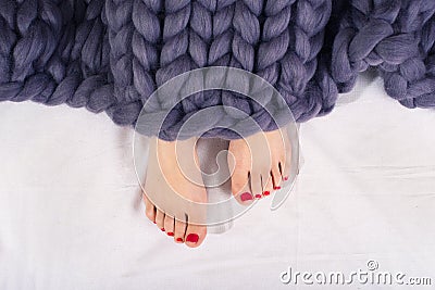 Woman feet under gray merino woolen plaid.Sleep under a warm knitted blanket. Stock Photo