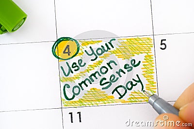 Woman fingers with green pen writing reminder Use Your Common Sense Day in calendar Stock Photo