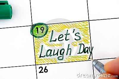 Woman fingers with pen writing reminder Lets Laugh Day in calendar Stock Photo