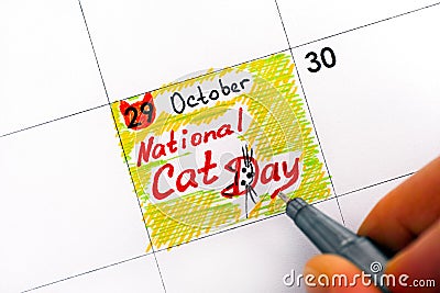 Woman fingers with pen writing reminder National Cat Day in calendar. Stock Photo