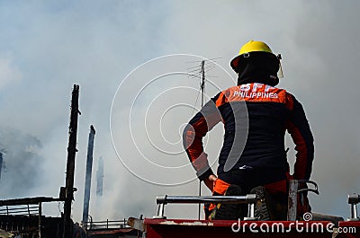 Woman Fire Fighter With Protective Hat sitting on top of fire truck in the area of burning house Editorial Stock Photo