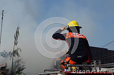 Woman Fire Fighter With Protective Hat sitting on top of fire truck in the area of burning house Editorial Stock Photo