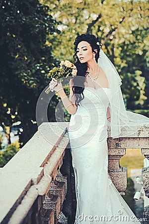 Woman with flowers on balcony. Sensual woman with wedding bouquet. Beauty girl with bridal makeup and hairstyle. Bride Stock Photo