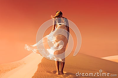 Woman in fluttering dress. Desert and sand dunes. Red sky. Stock Photo