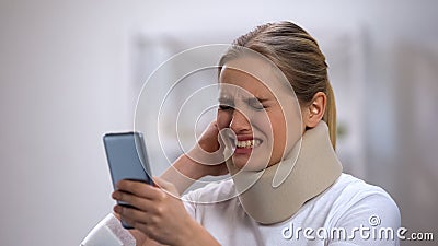 Woman in foam cervical collar reading message on phone feeling neck pain, injury Stock Photo