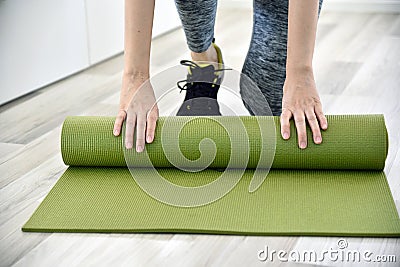 Woman folding yoga or fitness mat after working out at home. Stock Photo