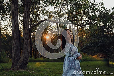 Woman alone in the forest at sunset with sunburst shining through trees Stock Photo