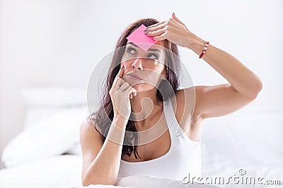 Woman forgetting something puts a pink post-it on her forehead, thinking Stock Photo