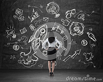 Woman in formal clothes who is looking at the wall with drawn business chalk icons. Stock Photo