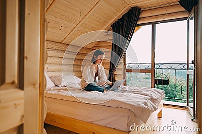 Woman freelancer in casual clothes working remotely on laptop in country wooden apartment. Female freelancer working online on Stock Photo