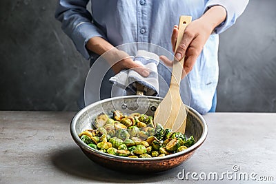 Woman with frying pan of roasted Brussels sprouts at table, closeup Stock Photo