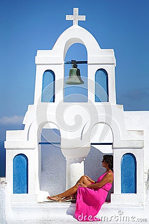 Woman with fuchsia dress sits in the bell tower of a small church in Oia in Santorini Stock Photo