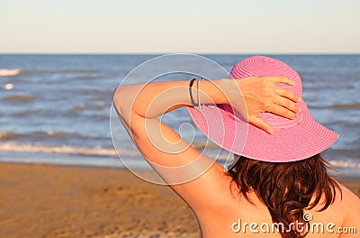 Woman with fuchsia hat on head waiting by the ocean Stock Photo