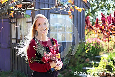 Woman Gardener in a Cottage Garden Holding Flowers in front of Shed Stock Photo