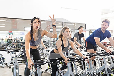 Woman Gesturing Victory While Exercising On Spinning Bike In Gym Stock Photo