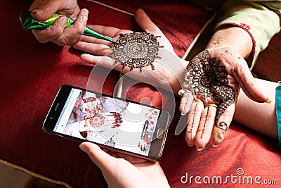 Woman getting a henna tattoo mehendi design copied from phone onto her hand for the bride bridesmaid shaadi event or a Stock Photo