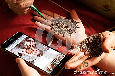 Woman getting a henna tattoo mehendi design copied from phone onto her hand for the bride bridesmaid shaadi event or a Stock Photo