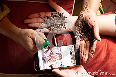 Woman getting a henna tattoo mehendi design copied from phone onto her hand for the bride bridesmaid shaadi event or a Stock Photo