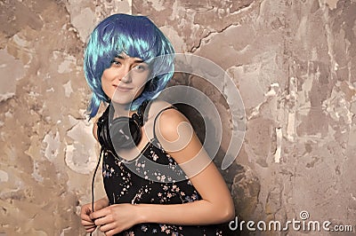 Woman in blue wig smiling with headphones on cement wall Stock Photo