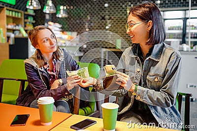 Woman gives to a stranger person or her friend euro banknote money in the interior of a cafe. The concept of lending money or Stock Photo
