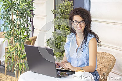 Woman in glass working remotely with laptop and phone in cafe. Beautiful brunette using notebook in cafe. Happy businesswoman call Stock Photo