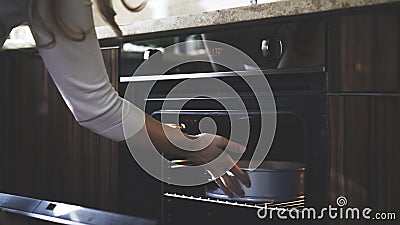 In the kitchen a woman puts a container into an oven Stock Photo