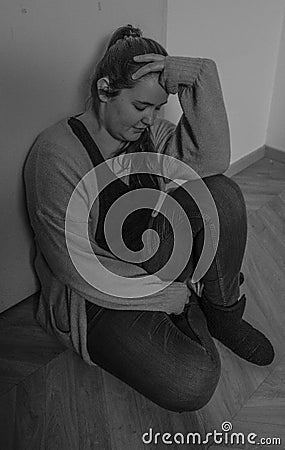 Woman is going through a difficult period, sitting with hands on her head against the door Stock Photo