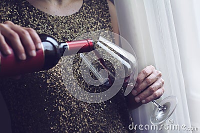 Woman with gold spangle dress pouring red wine into a glass Stock Photo