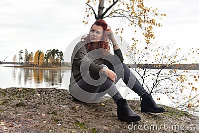 Woman in gray sits on stones by the lake in autumn Stock Photo