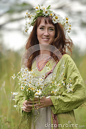 Woman in a green dress with a wreath of daisies in her hair and a bouquet of daisies in her hands Stock Photo