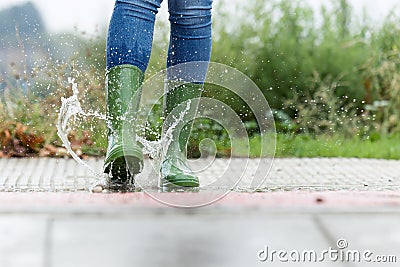 Woman in green rubber boots jumping on the puddle water in the street. Stock Photo