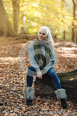 Woman in grey sweeter and jeans sitting in Autumn park Stock Photo