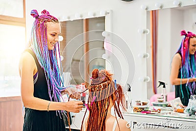 Woman hairdresser weaves to girl ginger dreadlocks. Stock Photo