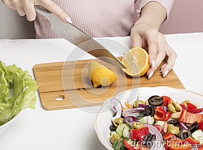 A woman halves a lemon on a cutting Board to add lemon juice to a Greek salad Stock Photo