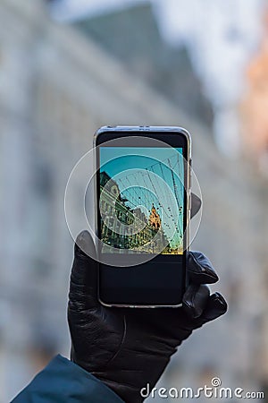 Woman hand a black leather glove holding black smartphone for taking picture of christmas city in a sunny day Stock Photo