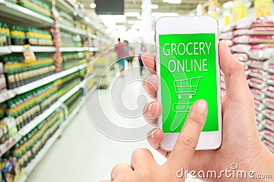 Woman hand click BUY NOW on mobile with blur supermarket background, Grocery online, delivery concept. Stock Photo