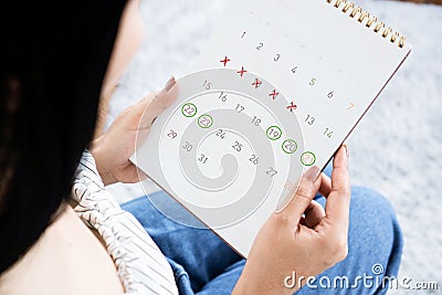 Asian woman hand holding calendar counting the date and checking her menstrual cycle planning for ovulation Stock Photo