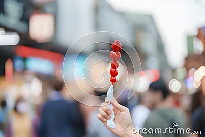 woman hand holding caramel coated strawberry skewer at night market. Street Food and travel concept Stock Photo