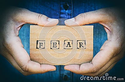 Woman hand holding cardboard card with word Fear. Denim backgrounds. Stock Photo