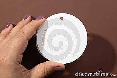 Woman hand holding cardboard white blank tag of round shape with little hole for clothes in upper part in center of Stock Photo