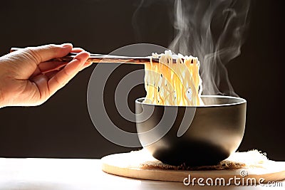 Woman hand holding chopsticks of instant noodles in cup with smoke rising dark background, Sodium diet high risk kidney Stock Photo