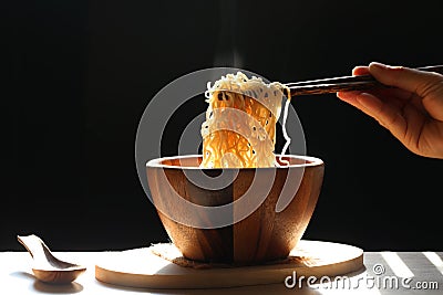 Woman hand holding chopsticks of instant noodles in cup with smoke rising dark background, Sodium diet high risk kidney failure, Stock Photo